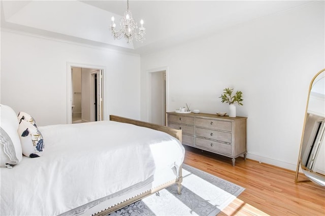 bedroom with an inviting chandelier, a tray ceiling, connected bathroom, and light hardwood / wood-style flooring