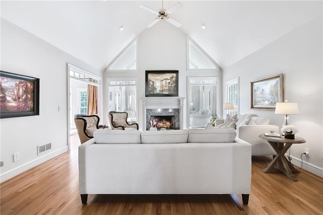 living room featuring a fireplace, high vaulted ceiling, ceiling fan, and light wood-type flooring