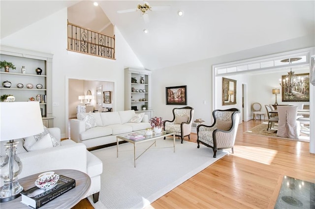 living room featuring high vaulted ceiling, hardwood / wood-style flooring, built in features, and ceiling fan with notable chandelier