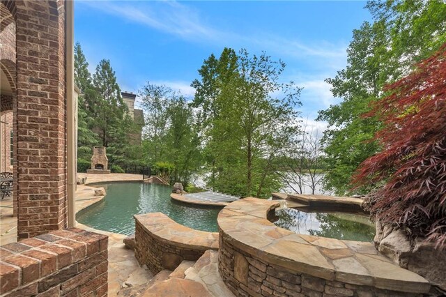 view of swimming pool featuring a brick fireplace, a pool with connected hot tub, and a patio area