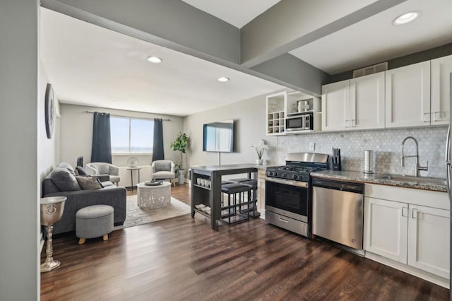 kitchen featuring stone countertops, decorative backsplash, appliances with stainless steel finishes, dark wood-style flooring, and a sink