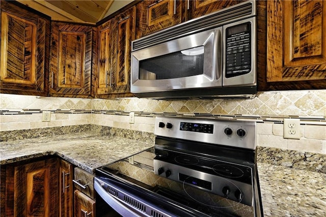 kitchen featuring light stone countertops, decorative backsplash, vaulted ceiling, and stainless steel appliances