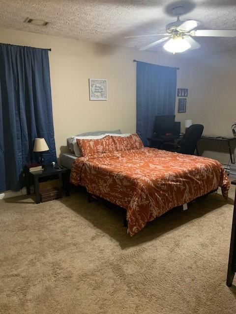 bedroom with ceiling fan, carpet flooring, and a textured ceiling