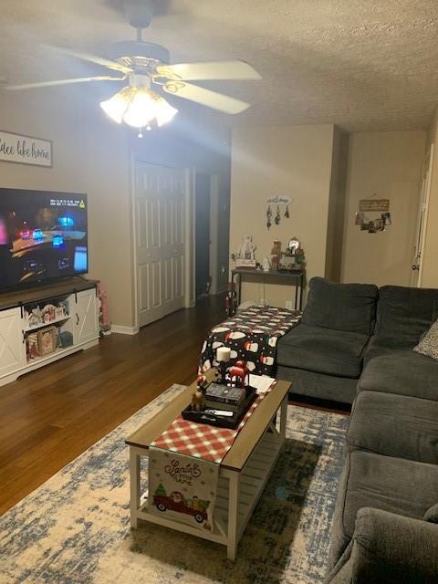 living room featuring dark wood-type flooring, ceiling fan, and a textured ceiling