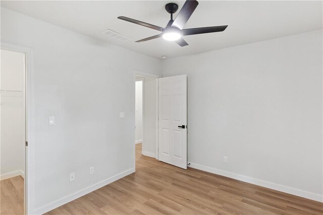 unfurnished bedroom with a walk in closet, light hardwood / wood-style flooring, a closet, and ceiling fan