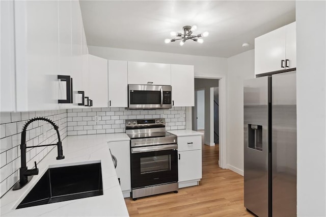 kitchen with sink, appliances with stainless steel finishes, light hardwood / wood-style floors, decorative backsplash, and white cabinets