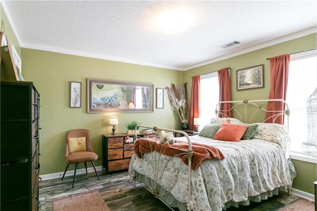 bedroom with a textured ceiling, baseboards, visible vents, crown molding, and wood finished floors