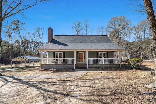 farmhouse with roof with shingles, a chimney, a porch, a detached carport, and driveway