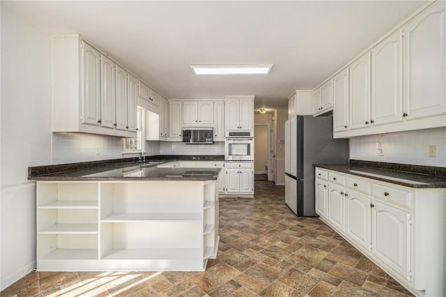 kitchen with appliances with stainless steel finishes, dark countertops, white cabinetry, and open shelves