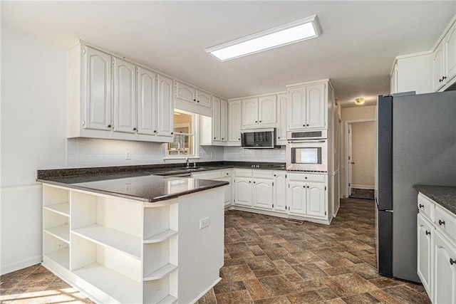 kitchen with white cabinets, dark countertops, appliances with stainless steel finishes, a peninsula, and open shelves