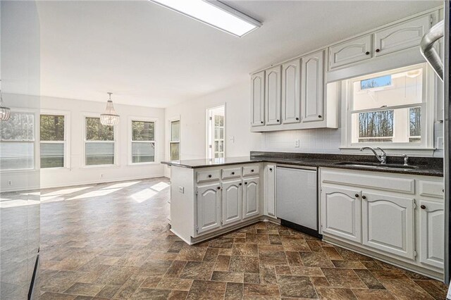 kitchen featuring dishwasher, dark countertops, a peninsula, pendant lighting, and a sink