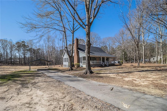 view of side of home featuring dirt driveway, a chimney, a porch, and a detached carport