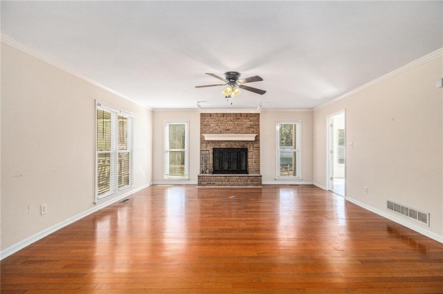 unfurnished living room featuring a healthy amount of sunlight, a brick fireplace, visible vents, and wood finished floors