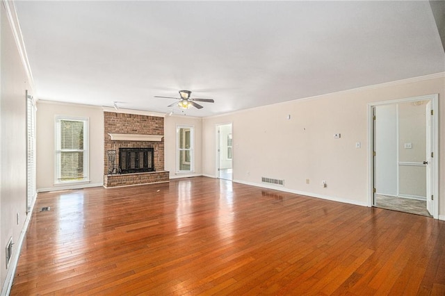 unfurnished living room featuring ceiling fan, a fireplace, wood finished floors, visible vents, and ornamental molding