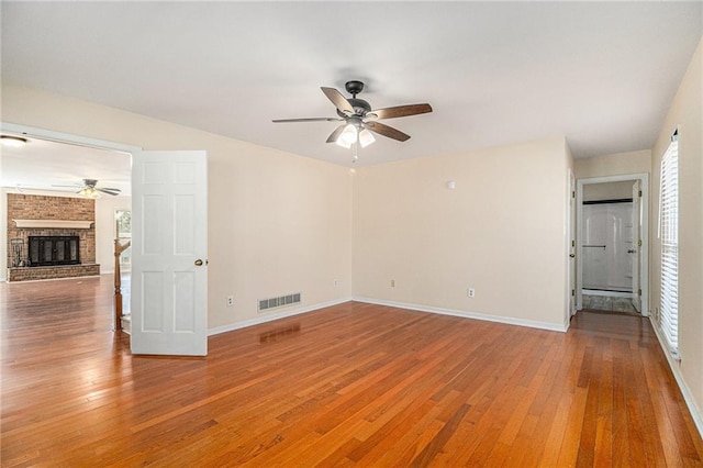 spare room featuring a fireplace, wood finished floors, visible vents, and baseboards