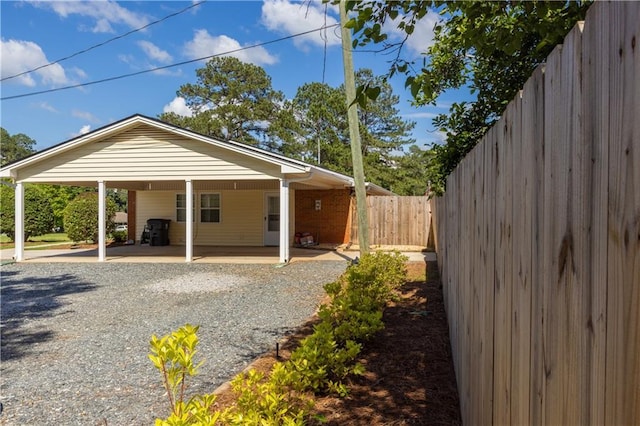 back of property featuring fence, a carport, and gravel driveway