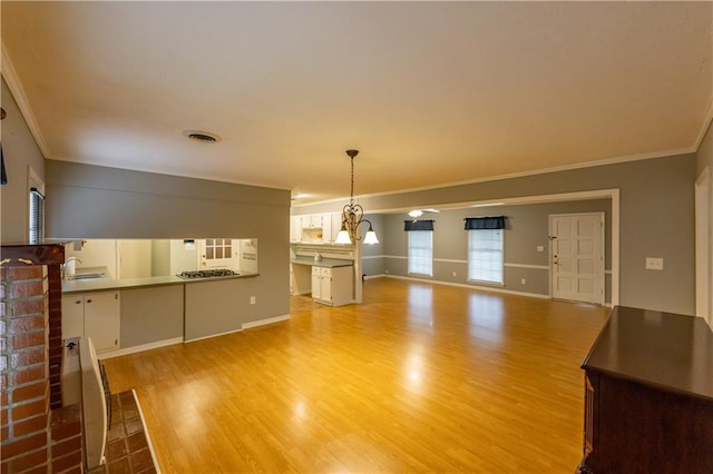 unfurnished living room featuring crown molding, light wood-style flooring, a sink, and baseboards