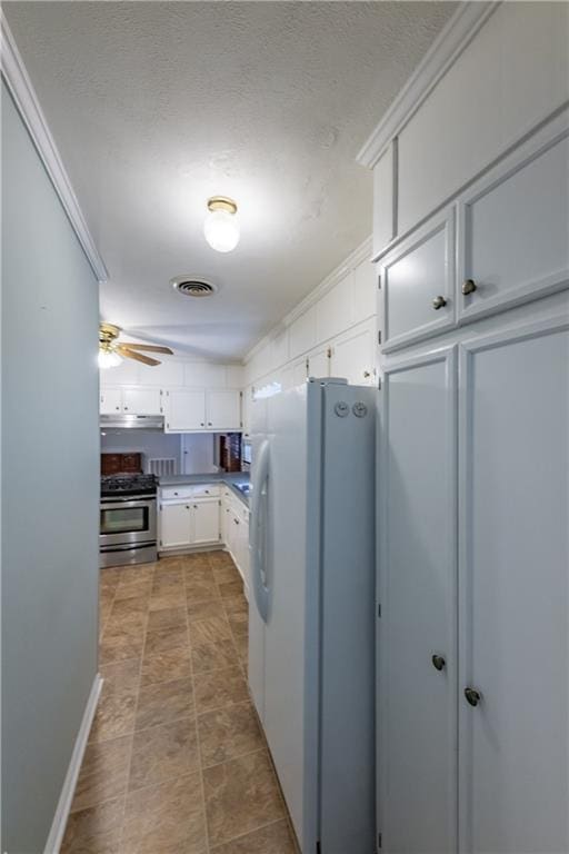 kitchen with freestanding refrigerator, stainless steel gas range, white cabinetry, under cabinet range hood, and ceiling fan