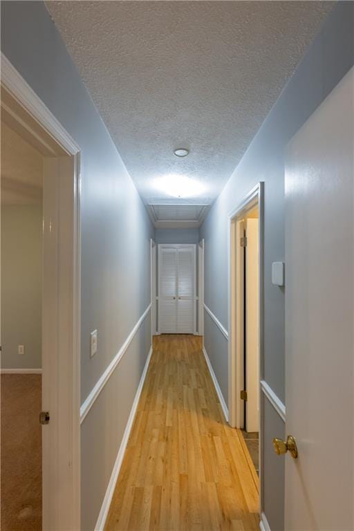 corridor featuring a textured ceiling, light wood-type flooring, and baseboards