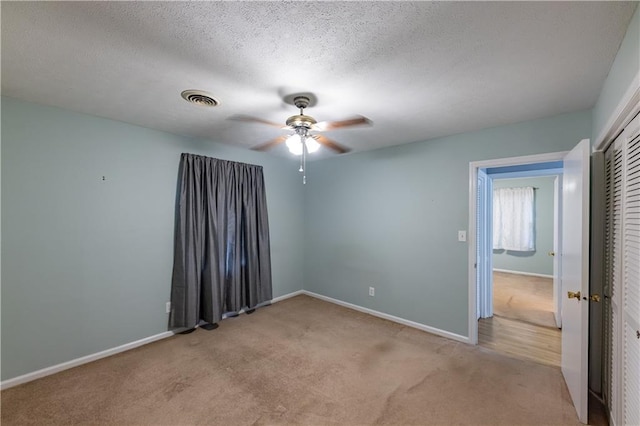 unfurnished room with light carpet, a ceiling fan, baseboards, and a textured ceiling