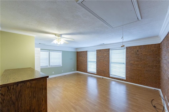 unfurnished living room with attic access, a textured ceiling, brick wall, baseboards, and light wood-style floors