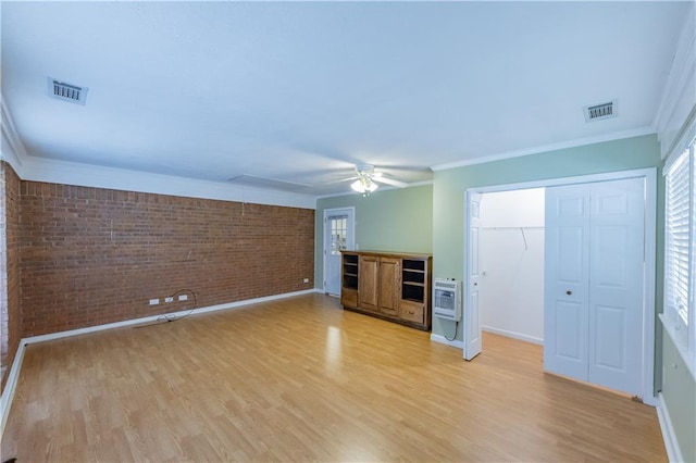 unfurnished living room featuring brick wall, light wood finished floors, ceiling fan, heating unit, and ornamental molding