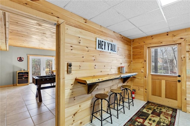 bar featuring tile patterned flooring, a healthy amount of sunlight, wooden walls, and french doors