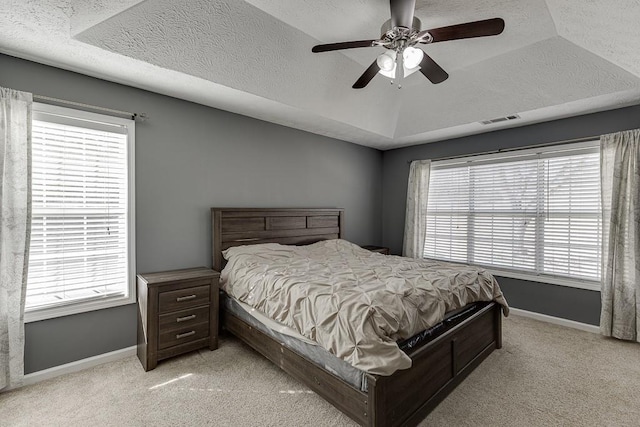 carpeted bedroom featuring a tray ceiling, multiple windows, and ceiling fan