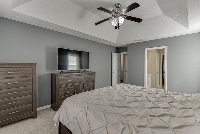 carpeted bedroom with a tray ceiling, ensuite bath, and ceiling fan