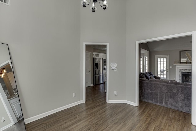 unfurnished living room with dark hardwood / wood-style flooring, a towering ceiling, a high end fireplace, and a chandelier