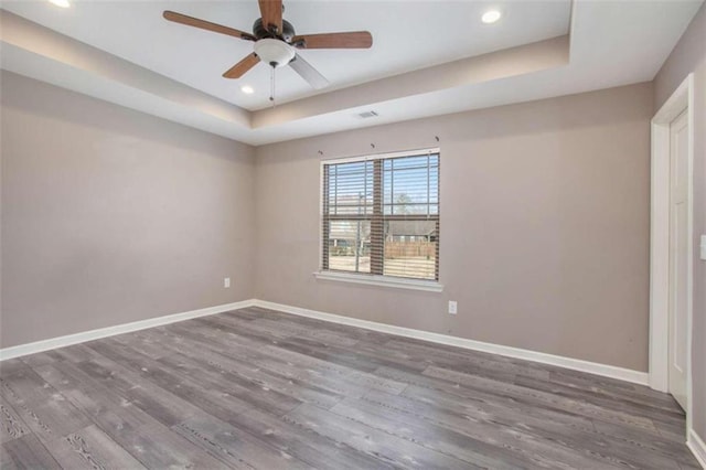 empty room featuring a raised ceiling, ceiling fan, and hardwood / wood-style flooring