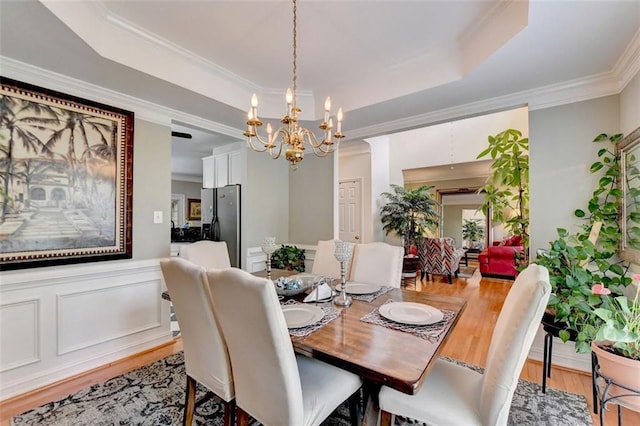 dining room featuring a raised ceiling, ornamental molding, hardwood / wood-style floors, and a chandelier