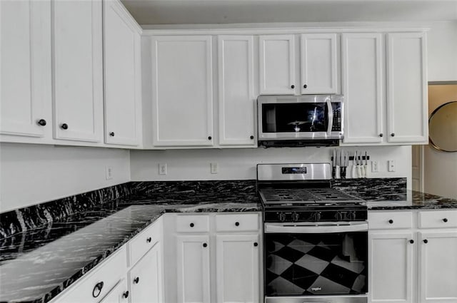 kitchen with stainless steel appliances, dark stone counters, and white cabinets