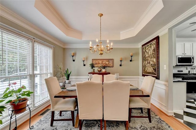 dining room featuring light hardwood / wood-style floors, a raised ceiling, a notable chandelier, and a healthy amount of sunlight