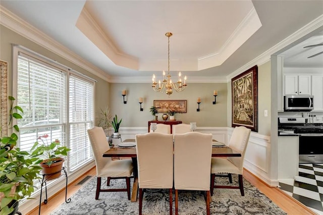 dining area with a raised ceiling, light wood-type flooring, and a chandelier