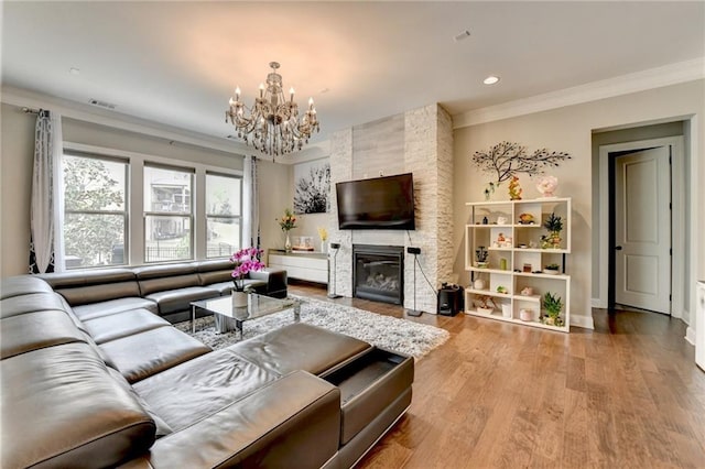 living area featuring visible vents, a chandelier, wood finished floors, a large fireplace, and crown molding
