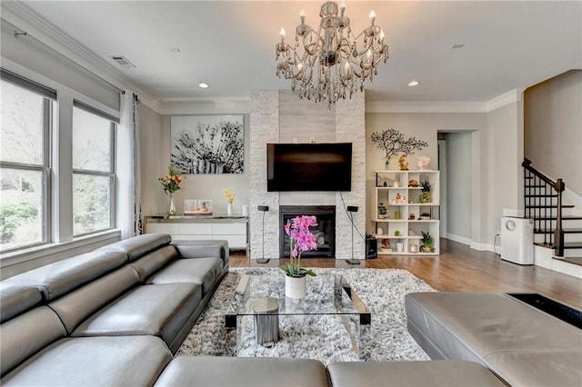 living room featuring stairs, wood finished floors, a chandelier, a large fireplace, and ornamental molding