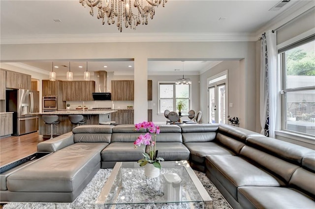 living area with a wealth of natural light, light wood-style flooring, an inviting chandelier, and crown molding