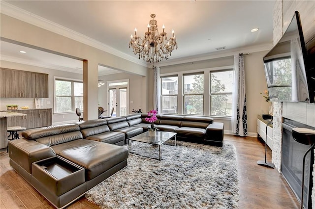 living area with wood finished floors, an inviting chandelier, baseboards, ornamental molding, and visible vents