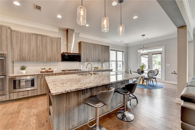 kitchen with modern cabinets, wall chimney range hood, a sink, and visible vents