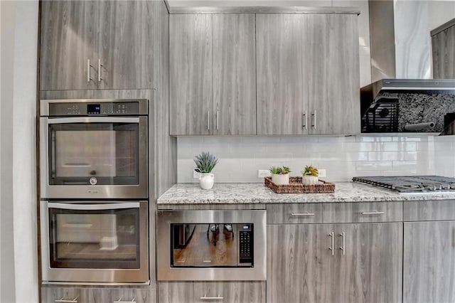 kitchen with modern cabinets, wall chimney exhaust hood, light stone counters, and stainless steel appliances