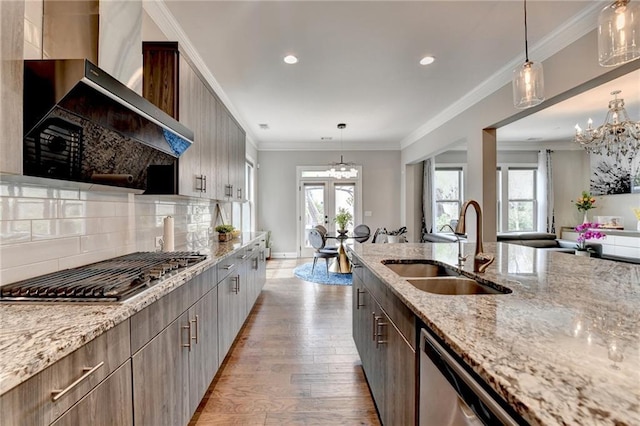 kitchen with wall chimney exhaust hood, a sink, a healthy amount of sunlight, wood finished floors, and appliances with stainless steel finishes
