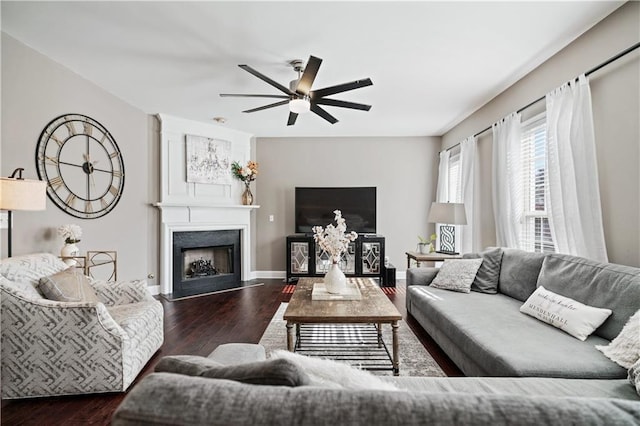 living area with a ceiling fan, a fireplace with flush hearth, baseboards, and wood finished floors