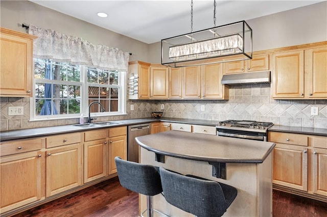 kitchen featuring dark countertops, appliances with stainless steel finishes, under cabinet range hood, light brown cabinets, and a sink