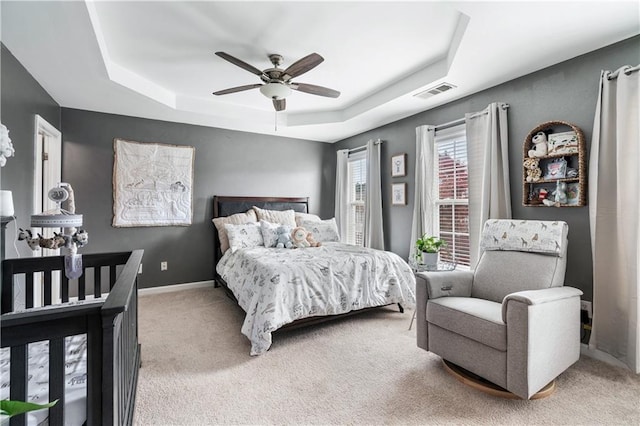 bedroom featuring light carpet, baseboards, visible vents, a raised ceiling, and ceiling fan