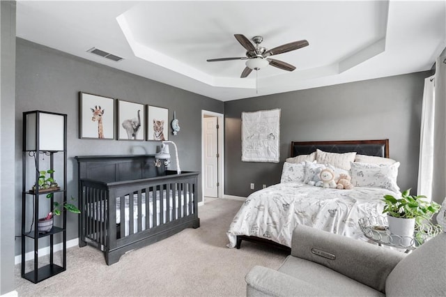 carpeted bedroom with a ceiling fan, a tray ceiling, visible vents, and baseboards