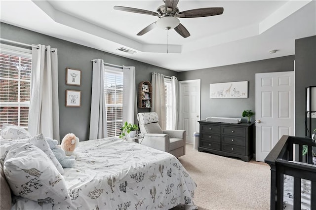 bedroom with carpet floors, visible vents, a raised ceiling, and a ceiling fan