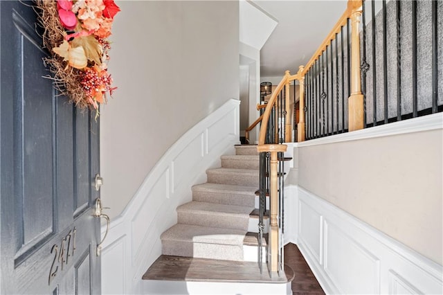 staircase with a wainscoted wall, wood finished floors, and a decorative wall