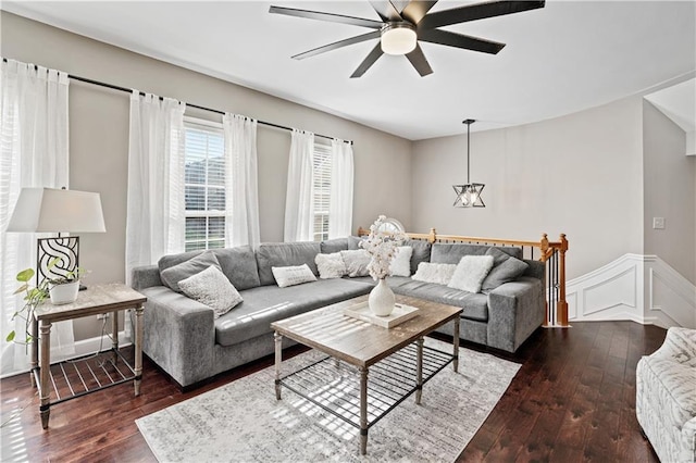 living area with ceiling fan with notable chandelier, hardwood / wood-style floors, wainscoting, and a decorative wall