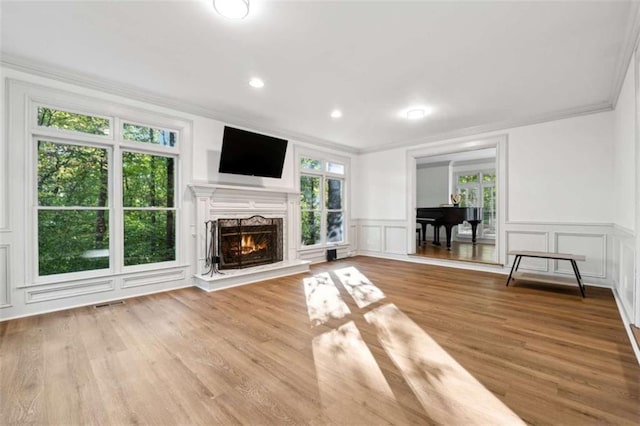 unfurnished living room with wood finished floors, visible vents, a lit fireplace, ornamental molding, and a decorative wall